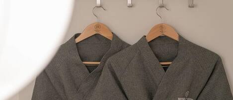 Two grey robes hanging on a wooden rack against a plain wall.