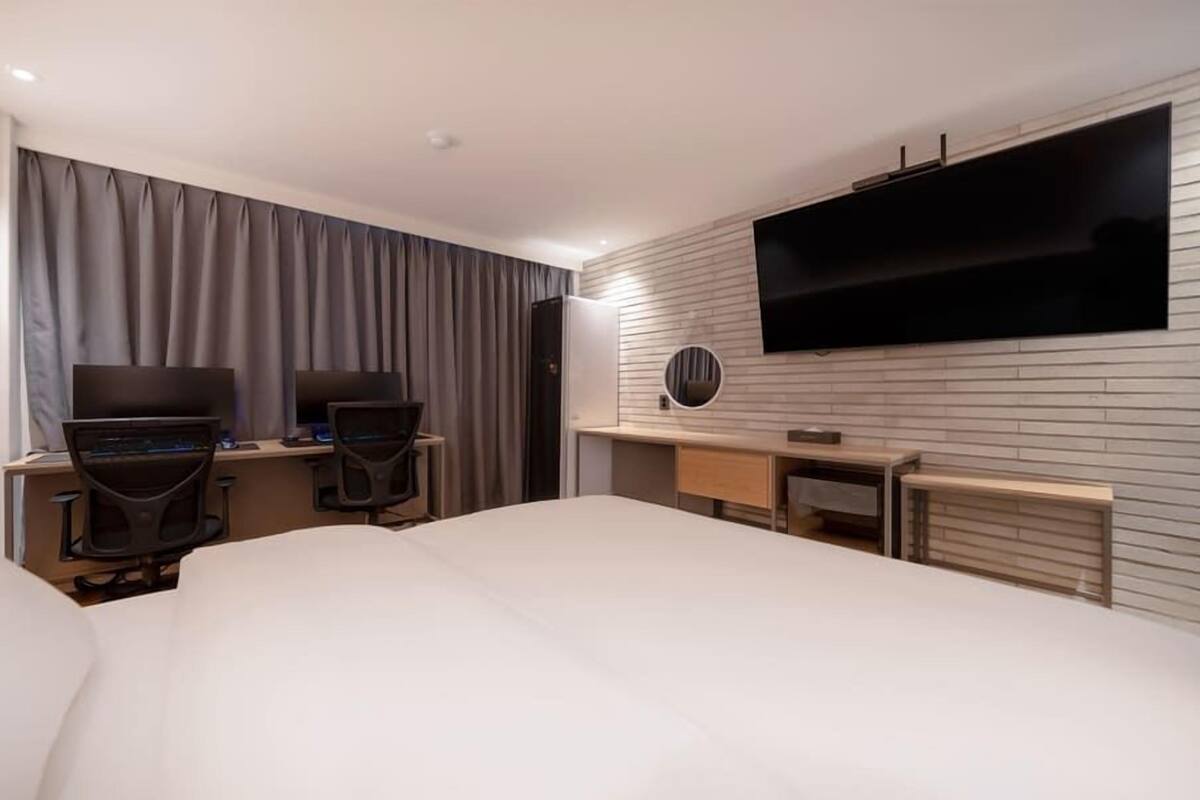 Een hotelkamer met een groot bed, twee bureaus met computers, een flatscreen televisie en een spiegel.