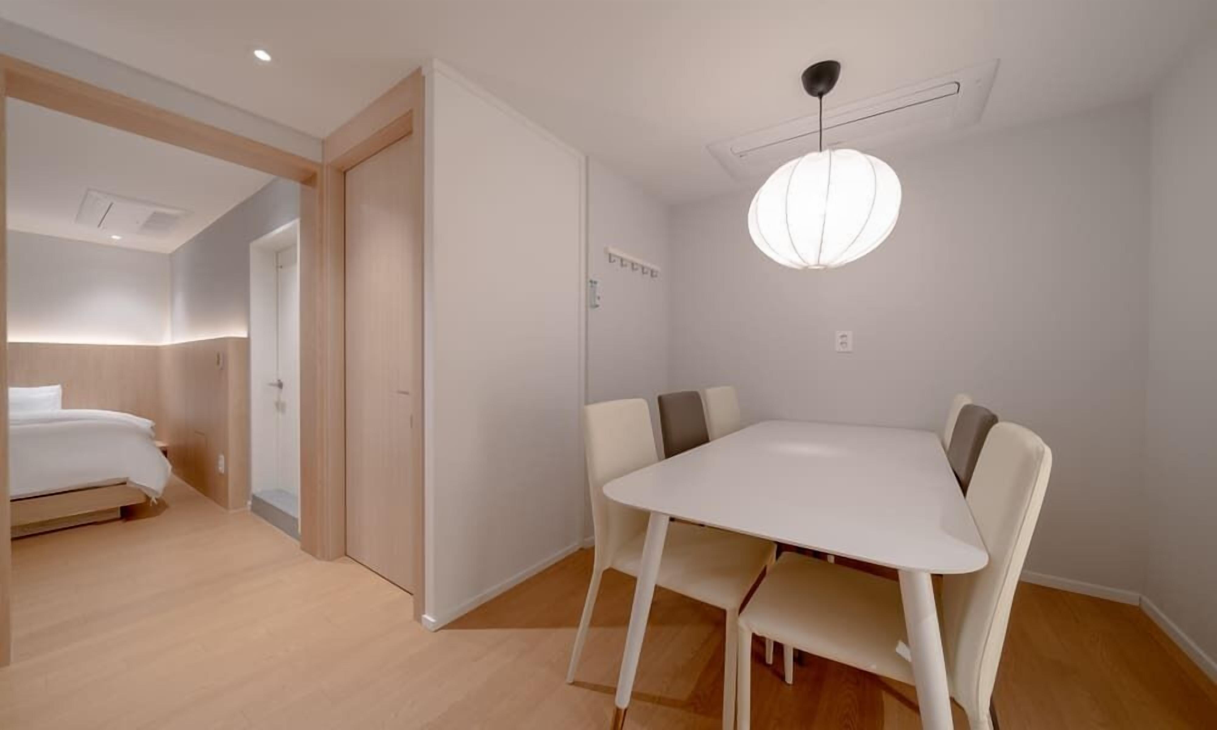 A modern hotel room with a bed, a small table with chairs, and a ceiling light fixture.