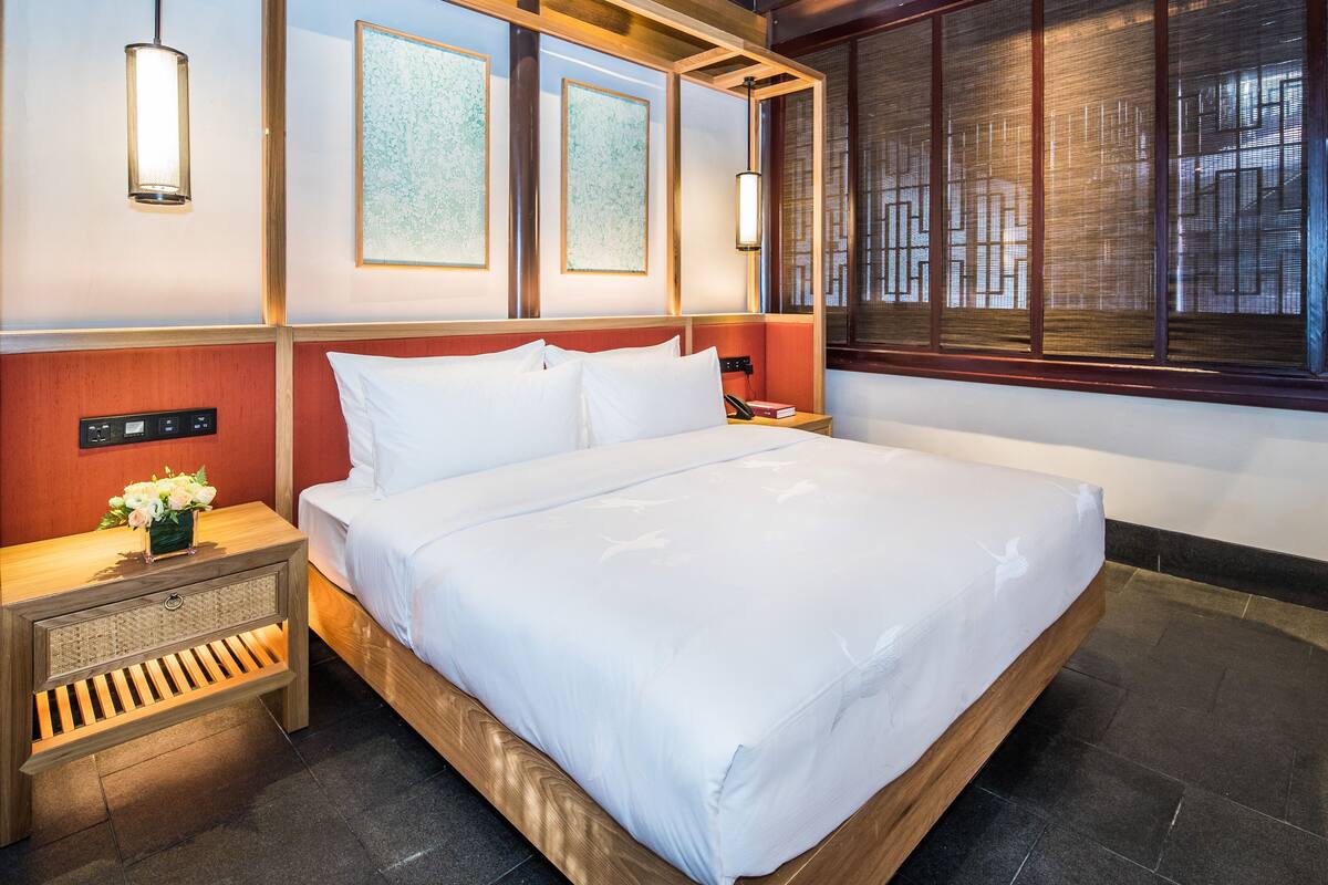 Habitación de hotel con una cama grande, cabecera de madera, mesitas de noche con lámparas y cuadros en las paredes.