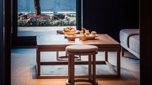 Una habitación japonesa tradicional con suelo de tatami, una mesa baja con cojín, una lámpara colgante y vistas a un árbol y un diseño de ventana geométrico.