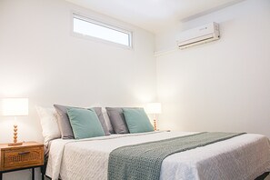 A bedroom with a bed, two bedside tables, a window, and an air conditioning unit. - Blue Vista - Paradise in Nettle Bay (Collectivité de Saint-Martin)