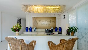 Een ontvangstgebied met een bordje voor The Kanjeng Suites & Villas in Sanur, Bali. Er staan rieten stoelen, een glazen balie en decoratieve vazen.
