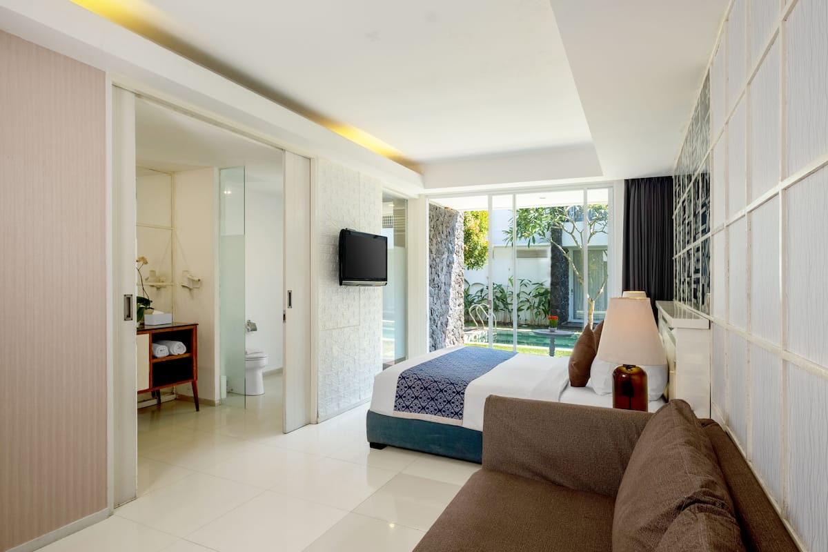 Habitación de hotel moderna con cama, sofá, televisión y vista a una piscina.