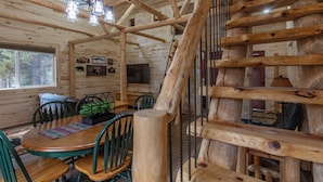 A wooden cabin interior with a dining area, a staircase, and a television.