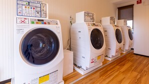 A row of white front-loading washing machines in a laundry room with wooden flooring and vertical striped wallpaper. - HOTEL R9 The Yard Kawaminami (Kawaminami)