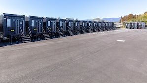 A row of portable restrooms with numbered doors, a paved parking area, and a building in the background. - HOTEL R9 The Yard Kawaminami (Kawaminami)