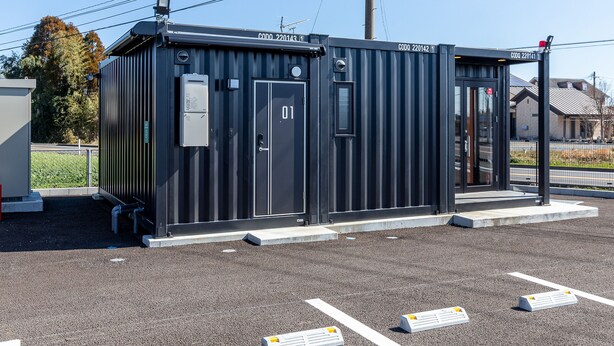A small, dark-colored portable restroom with a door labeled "01" and a sign above it. - HOTEL R9 The Yard Kawaminami (Kawaminami)