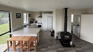 A modern kitchen with a central island, a built-in stove, and a large window providing a view of the outdoors. - Peaceful riverfront cottage in tiny northland town (Te Kopuru)