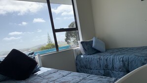 A room with two beds, one with a floral-patterned bedspread and the other with a solid color. There is a window providing a view of trees and hills. - Peaceful riverfront cottage in tiny northland town (Te Kopuru)