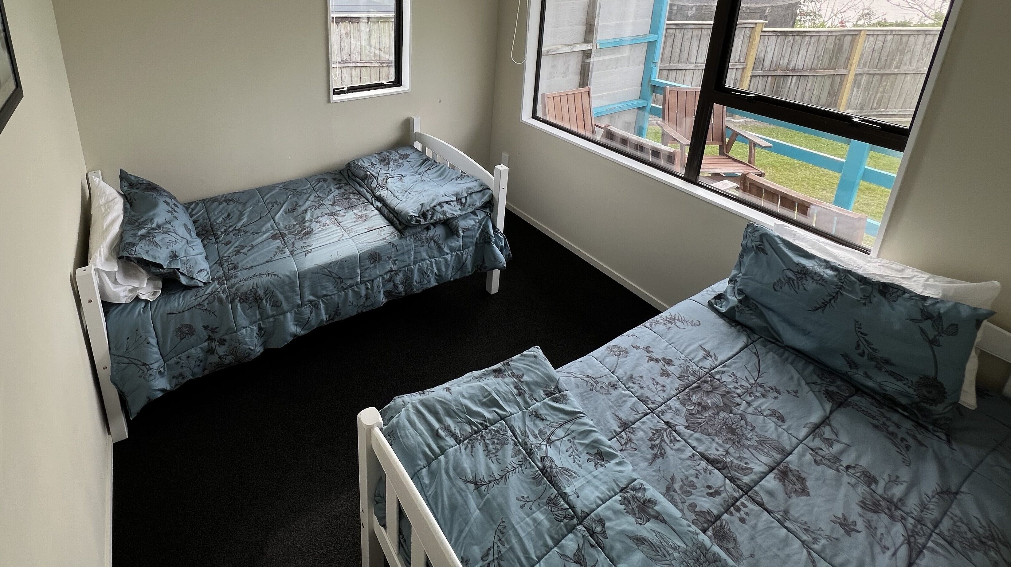 A small room with two single beds, a window, and a view of a backyard.