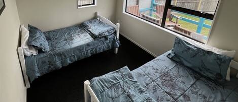 A small room with two single beds, a window, and a view of a backyard.