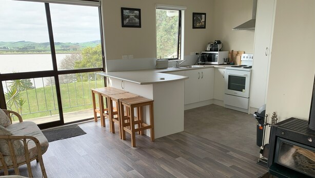 A modern kitchen with a large island, white cabinets, and a view of the outdoors. - Peaceful riverfront cottage in tiny northland town (Te Kopuru)