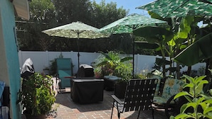 Ein Patio mit Backsteinfassade, Gartenmöbeln und Sonnenschirmen, die Schatten spenden.