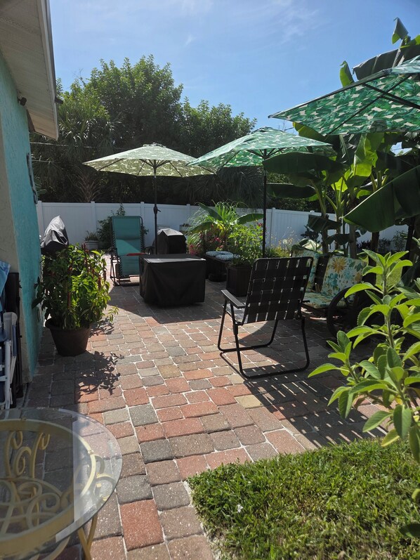 A patio area with a brick floor, outdoor furniture, and umbrellas providing shade.
