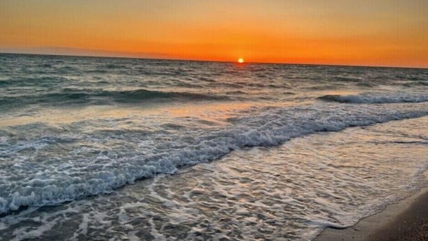 Ein Sonnenuntergang über dem Meer, wobei Wellen auf die Küste zulaufen.