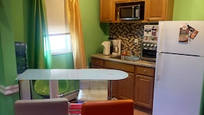 A compact kitchen with wooden cabinets, a white refrigerator, and a small dining area with a table and two chairs. - Cozydelightful near UBS ARENA, JFK, LAGUARDIA AIRPORT.  (Queens)