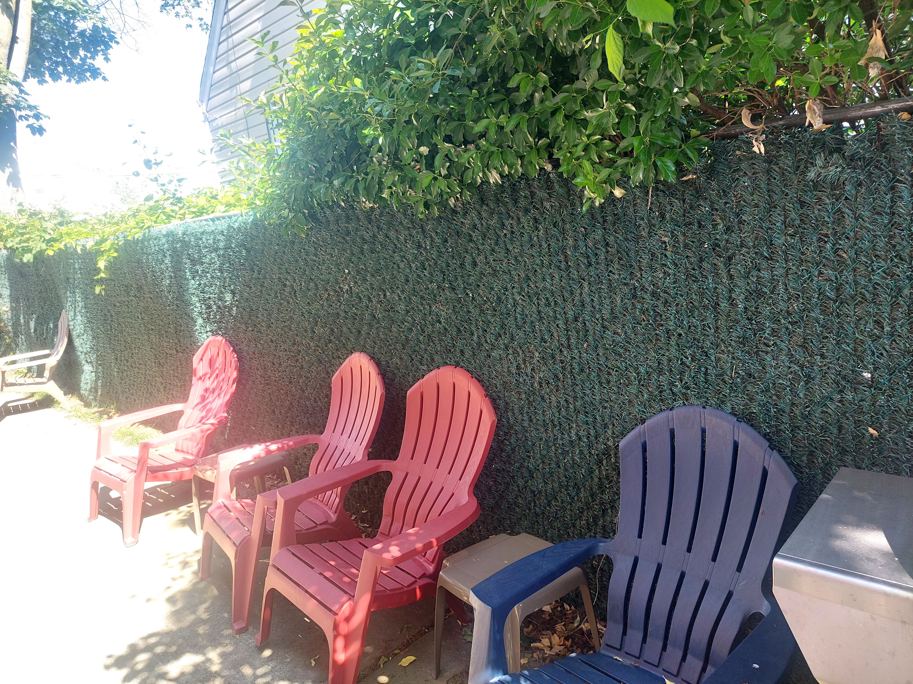 Outdoor seating with chairs and a table, surrounded by a hedge and a building.