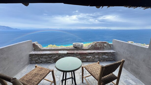 A balcony with a table and two chairs overlooking a coastal view.