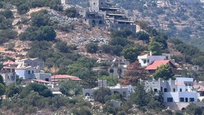 A coastal village with stone buildings, some with red roofs, and a prominent tower structure on a hillside.