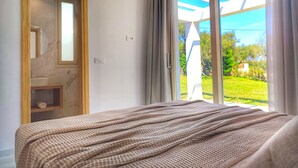 A bedroom with a large bed, a wooden door, and a view of greenery through a glass door. - Fence off , surrounded by large olive grove 200m from the sandy beach (Ζάκυνθος)