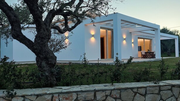 A modern house with a white exterior, large windows, and a stone wall in the foreground. - Fence off , surrounded by large olive grove 200m from the sandy beach (Ζάκυνθος)