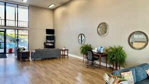 A spacious living area with a large window, a grey sofa, a wooden floor, and a desk with a laptop. - Big Chile Inn & Suites (Las Cruces)