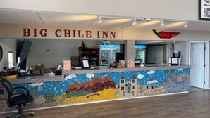 A reception desk at the Big Chile Inn with a mosaic mural, a refrigerator, and a chair. - Big Chile Inn & Suites (Las Cruces)