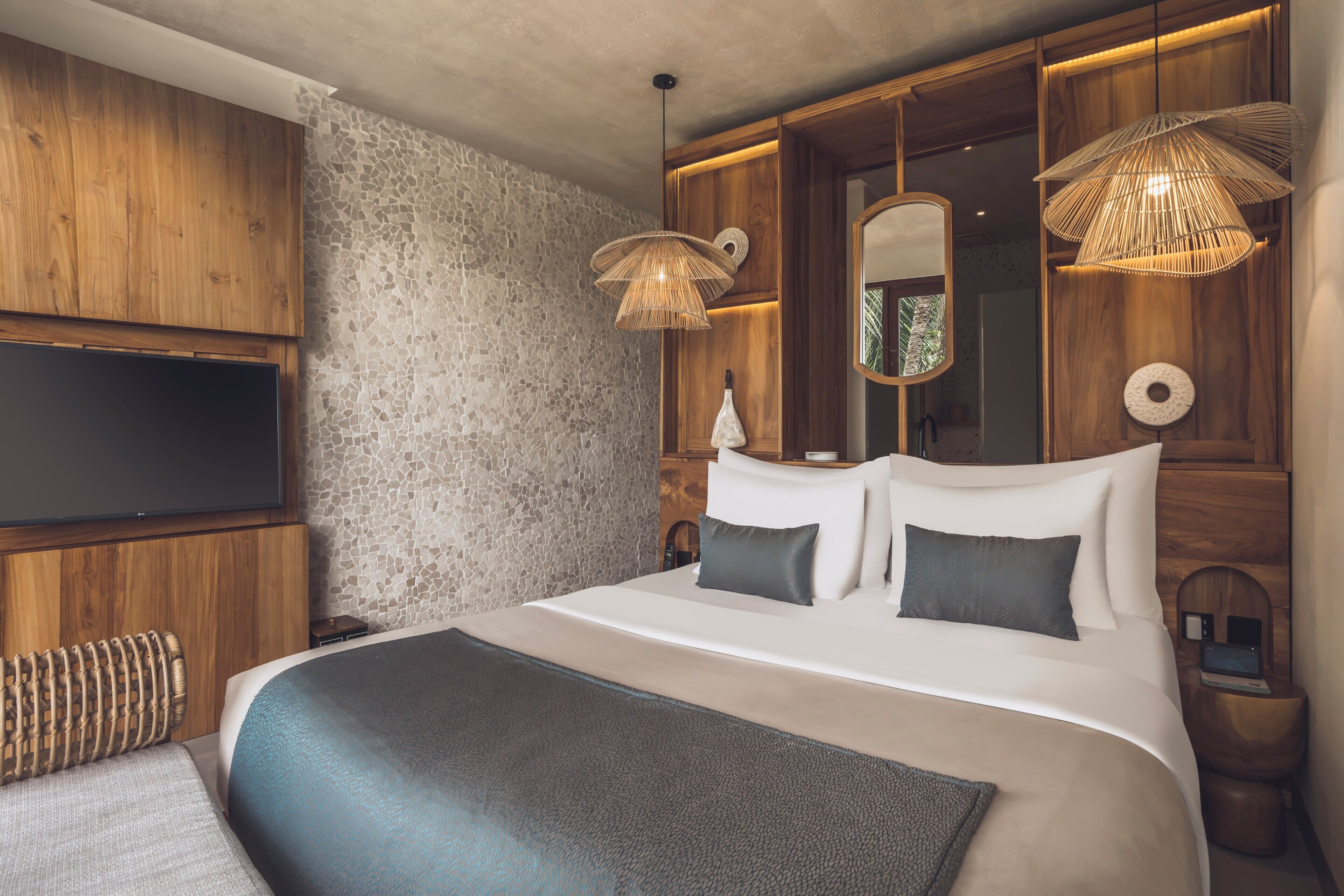 A modern bedroom with a large bed, wooden headboard, a flat-screen TV, and two pendant lights.