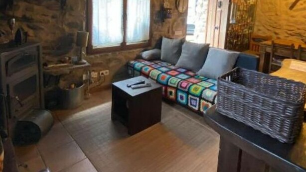 Una habitación rústica con paredes de piedra, techo de madera, un sofá acogedor, chimenea y un ventanal grande.