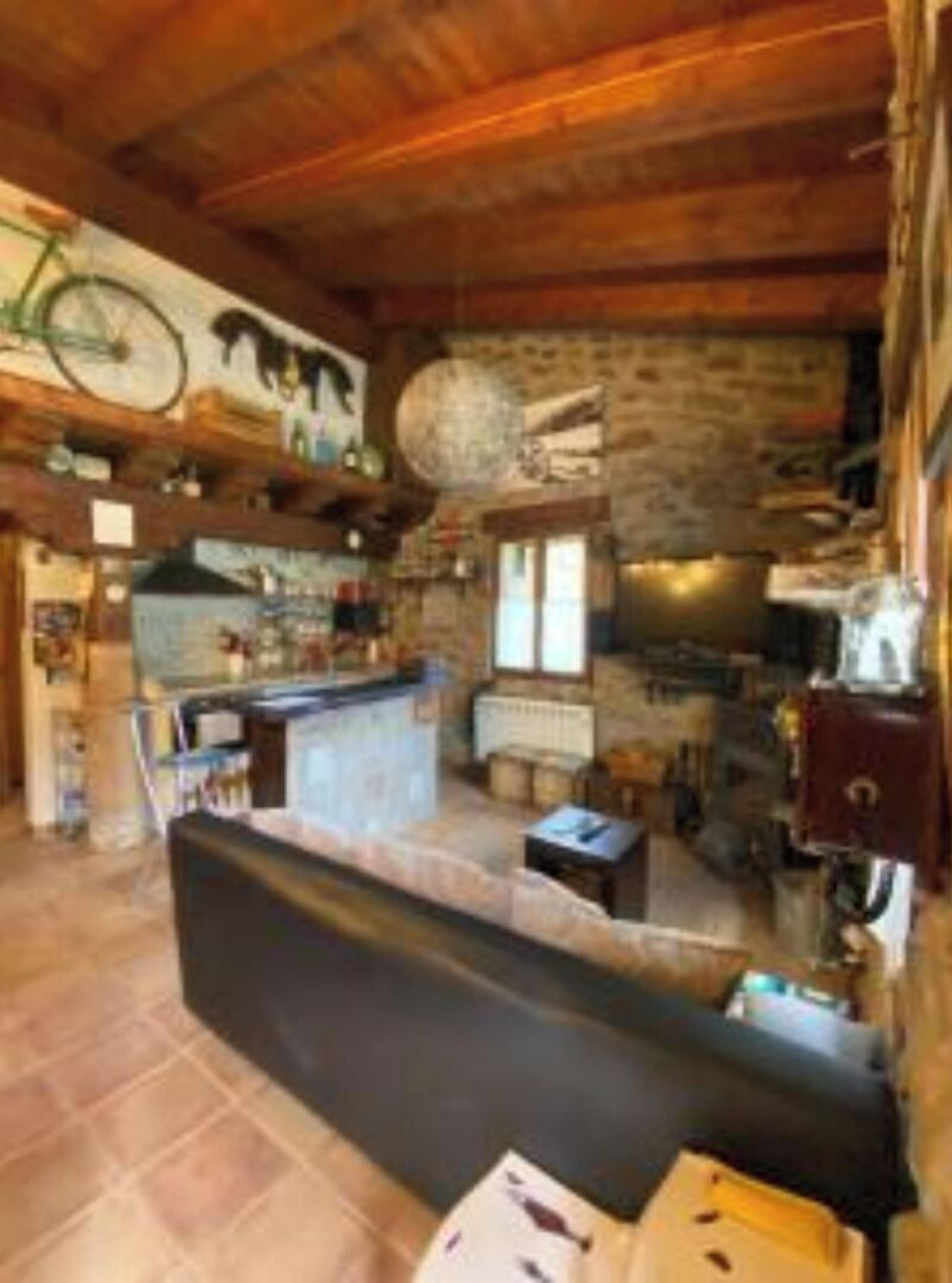 A rustic cabin interior with a stone wall, wooden ceiling, a sofa, a kitchen area, and a bicycle mounted on the wall.