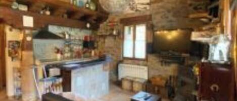 A rustic cabin interior with a stone wall, wooden ceiling, a sofa, a kitchen area, and a bicycle mounted on the wall.
