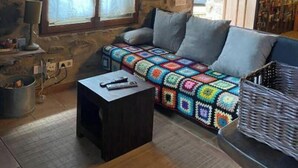 Una habitación acogedora con pared de piedra, techo de madera, una manta colorida en un sofá y una cesta sobre una mesa.