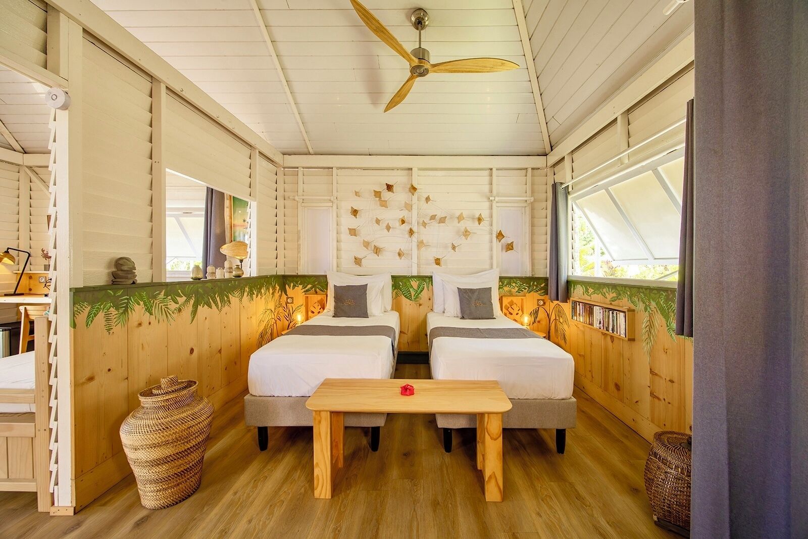 A cozy cabin-style room with two beds, a wooden ceiling fan, and a large window.