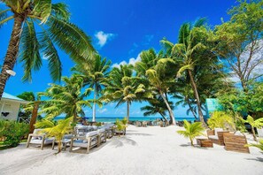Una playa con palmeras, sillas de descanso y un cielo azul despejado.