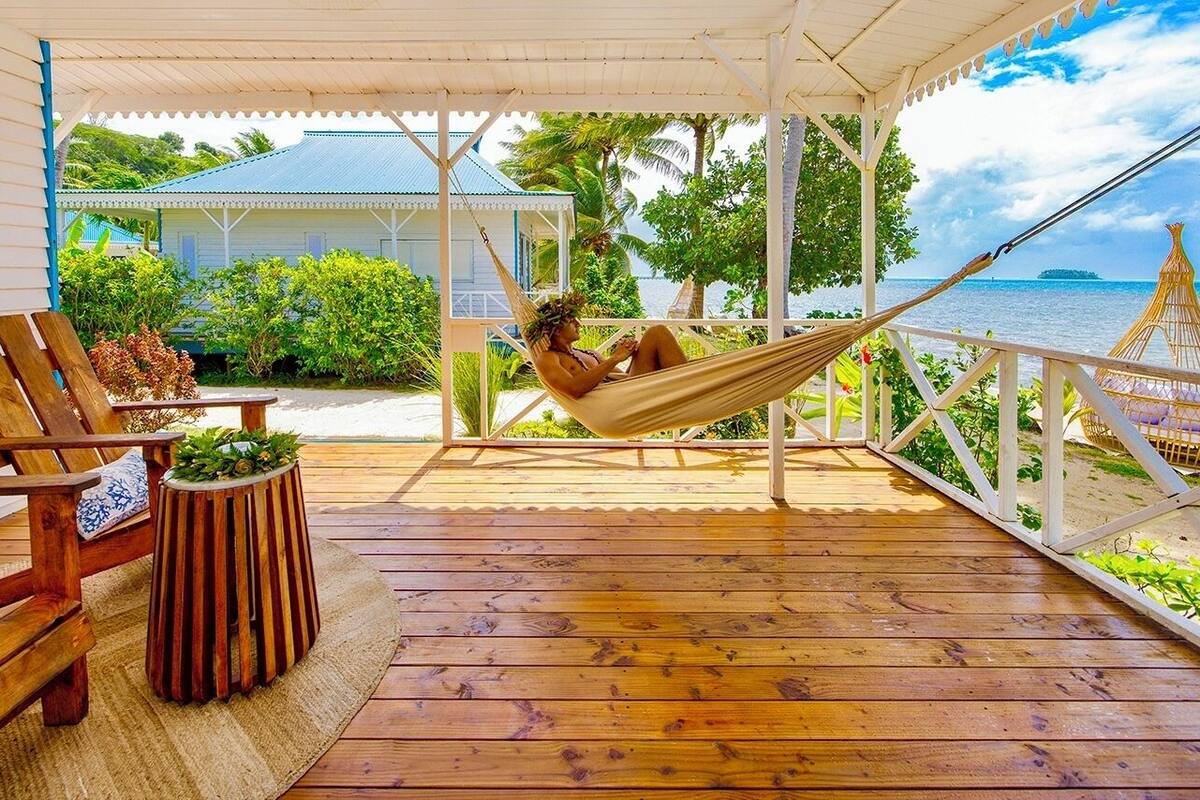A wooden deck with a hammock, chairs, and a small table with plants.