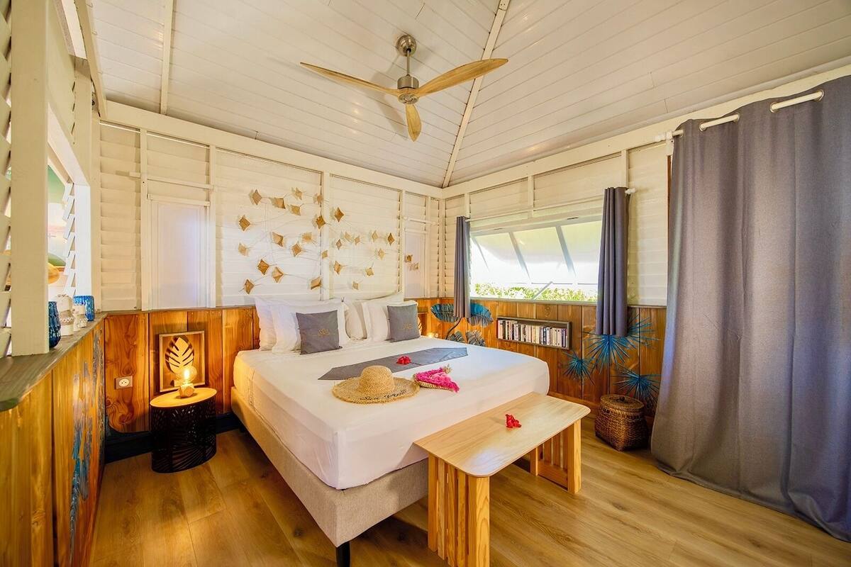 A bedroom with a bed, bedside table, ceiling fan, and a window with curtains.
