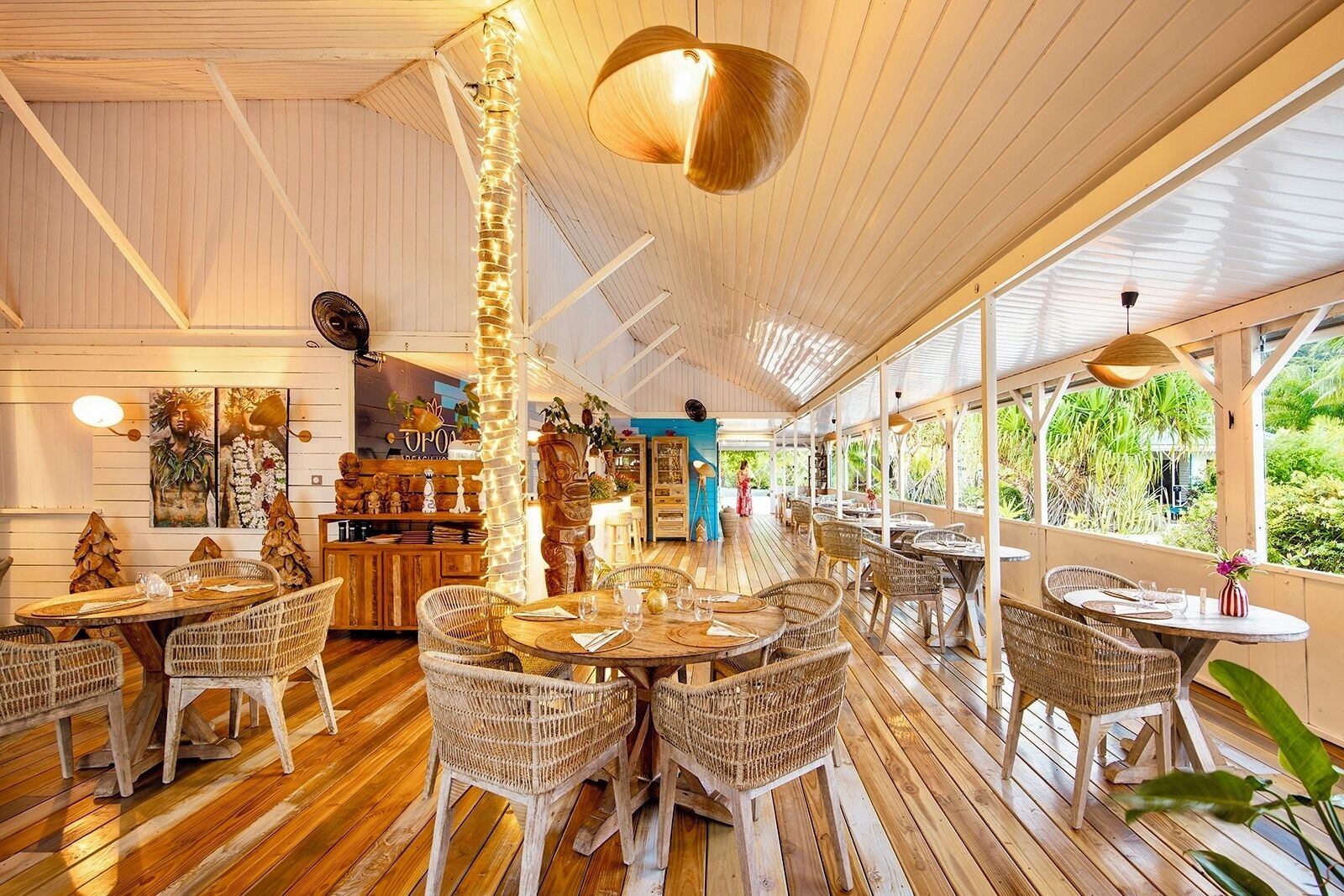 Un restaurante con suelos de madera, mobiliario de mimbre y amplios ventanales con vistas a la vegetación.