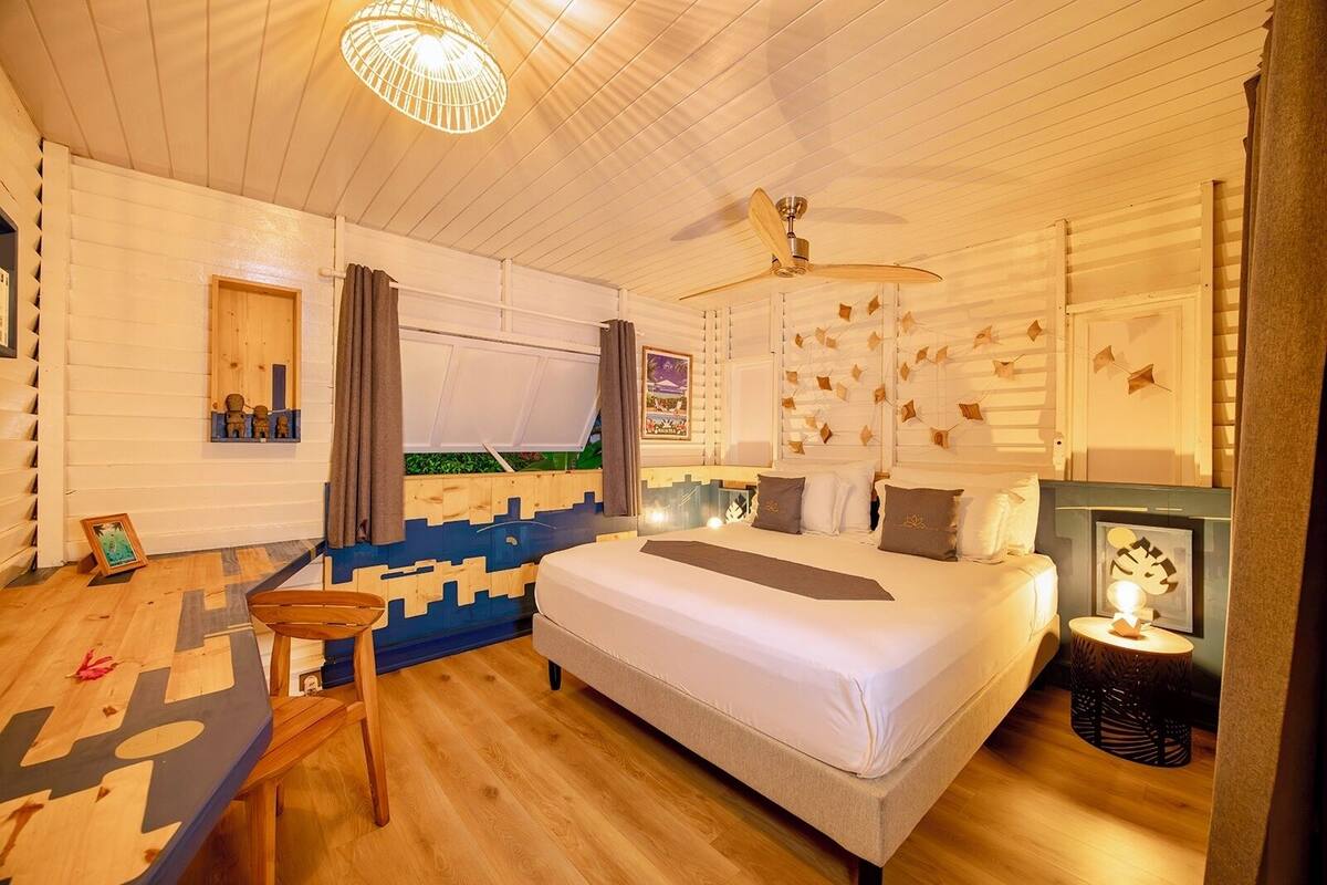 A cozy bedroom with a bed, a ceiling fan, a small table, and a nightstand.