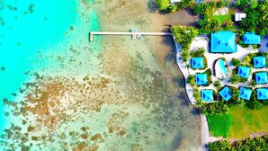 Une vue aérienne d’un complexe hôtelier avec de nombreux bâtiments aux toits bleus, une jetée s’avançant dans des eaux turquoise et une végétation luxuriante qui entoure l’ensemble.
