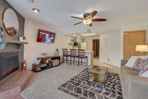 A living room with a fireplace, a ceiling fan, a TV mounted on the wall, and a kitchen area in the background. - Steph's Waterfront Retreat (Wisconsin Dells)