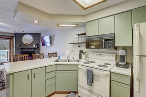 A compact kitchen with a stove, microwave, and refrigerator. There is a dining area with chairs and a TV mounted on the wall. - Steph's Waterfront Retreat (Wisconsin Dells)