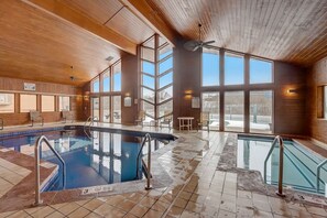 Une piscine intérieure avec des parois en verre transparent, un plafond en bois et un sol carrelé.