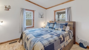 A bedroom with a wooden headboard, a quilted bedspread, two windows with curtains, a wall-mounted light, and a small decorative deer sticker. - 16 Acres of beauty and relaxation  (Park Hills)