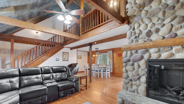 A spacious living room with a black leather sectional sofa, a stone fireplace, wooden beams, and a staircase. - 16 Acres of beauty and relaxation  (Park Hills)