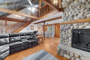 A spacious living room with a black leather sectional sofa, a stone fireplace, wooden beams, and a staircase. - 16 Acres of beauty and relaxation  (Park Hills)