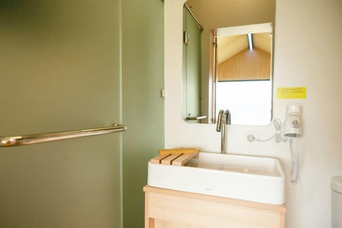 Un baño con lavamanos blanco, espejo, armario de madera, perchero y teléfono.
