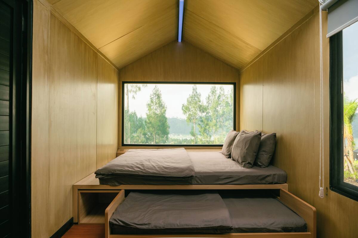 A compact bedroom with a large window, a bunk bed, and a small bedside table.