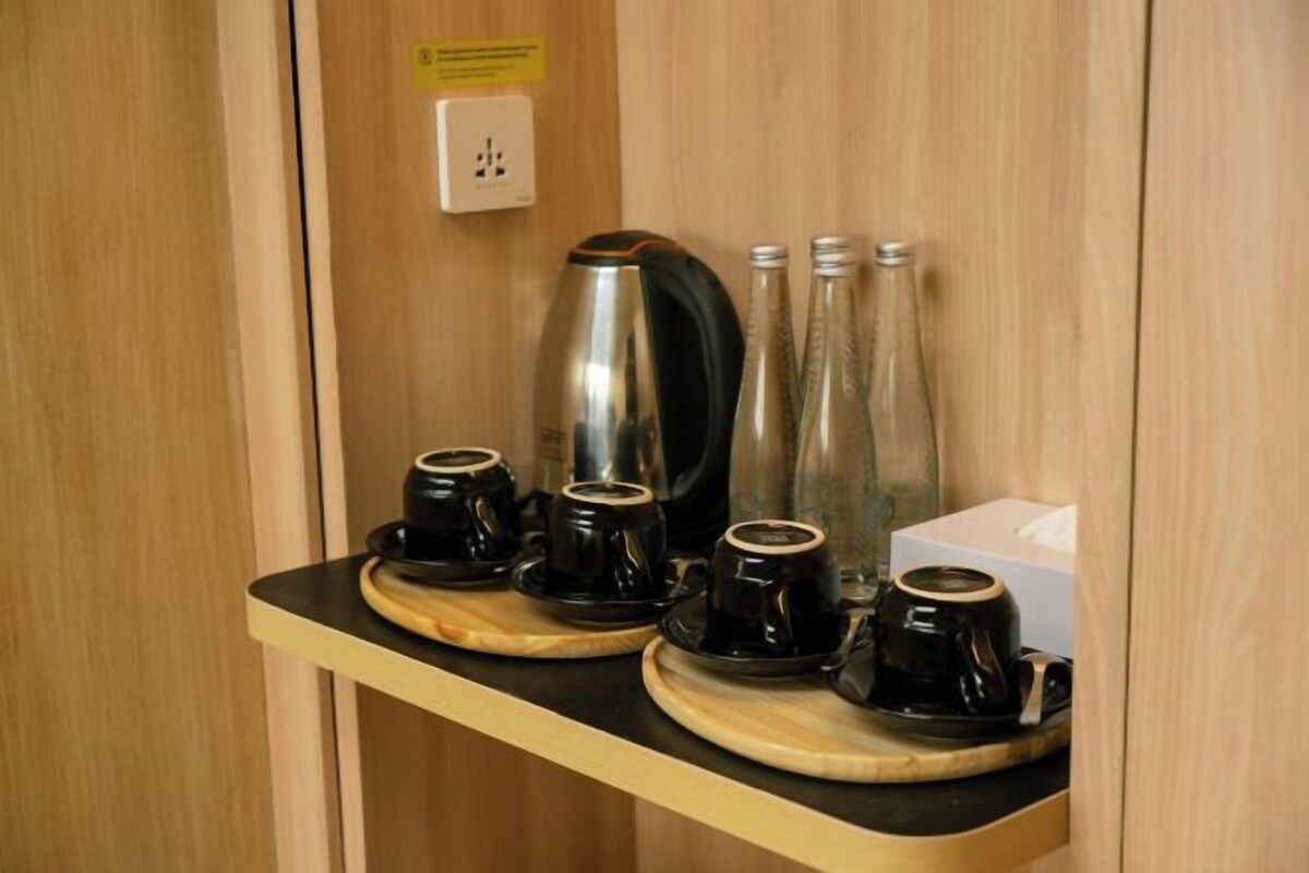 Una estación de café con cuatro tazas y platillos negros, una cafetera y tres botellas de vidrio sobre un estante de madera.