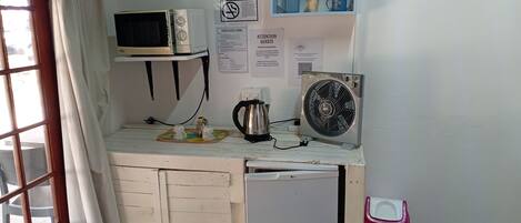 Una kitchenette con microondas, hervidor, ventilador y un refrigerador pequeño. Hay un letrero de 'No Fumar' y un letrero de 'Guest Farm' en la pared.